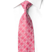 A pink necktie with a white floral pattern, styled in a knot on a white collared dress shirt against a white background.